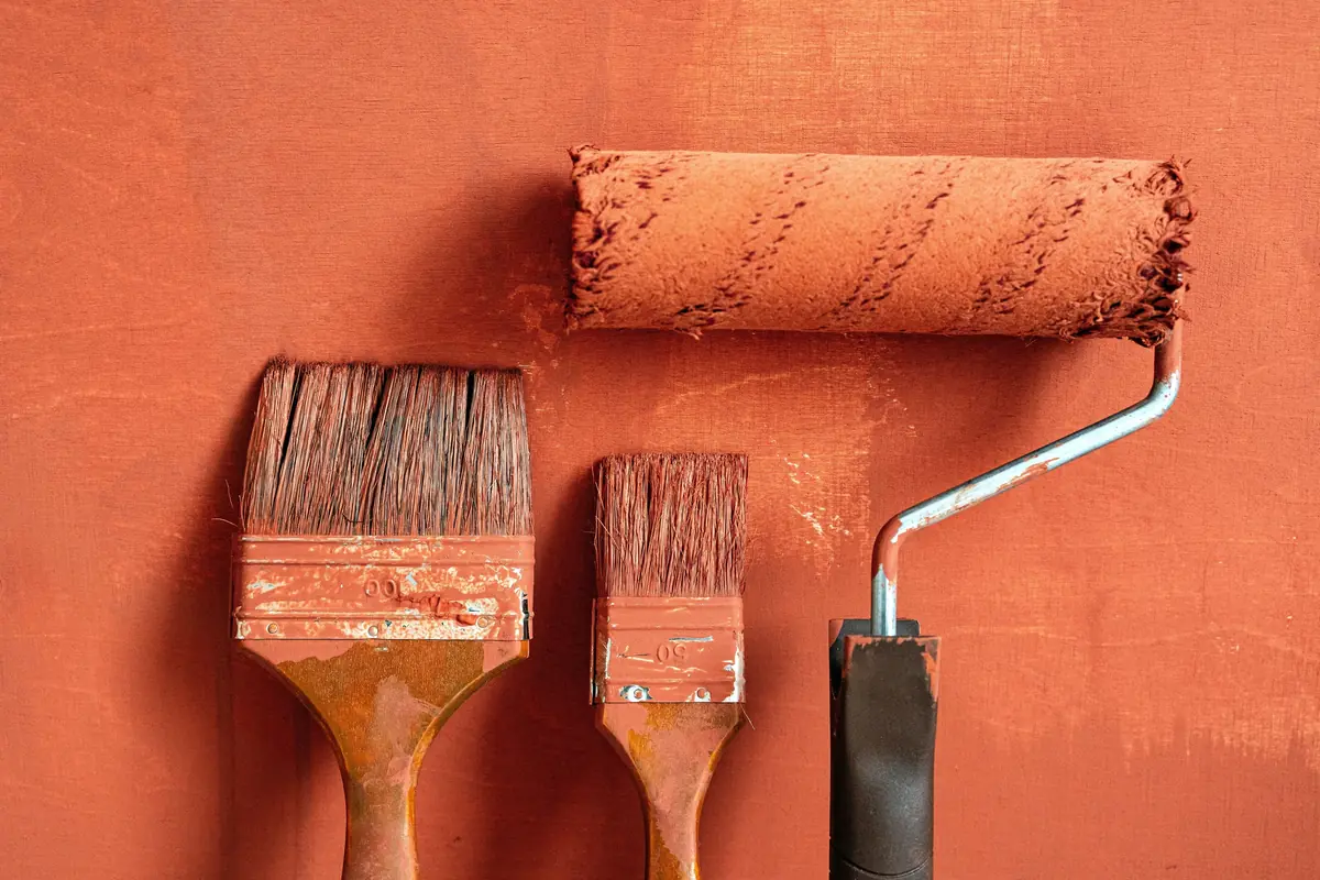 Brushes and a roller on a terracotta wall Two paint brushes and a roller resting against a freshly painted terracotta wall