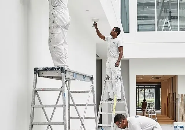 Painting a commercial interior Painters on ladders and a rolling platform in a bright commercial space