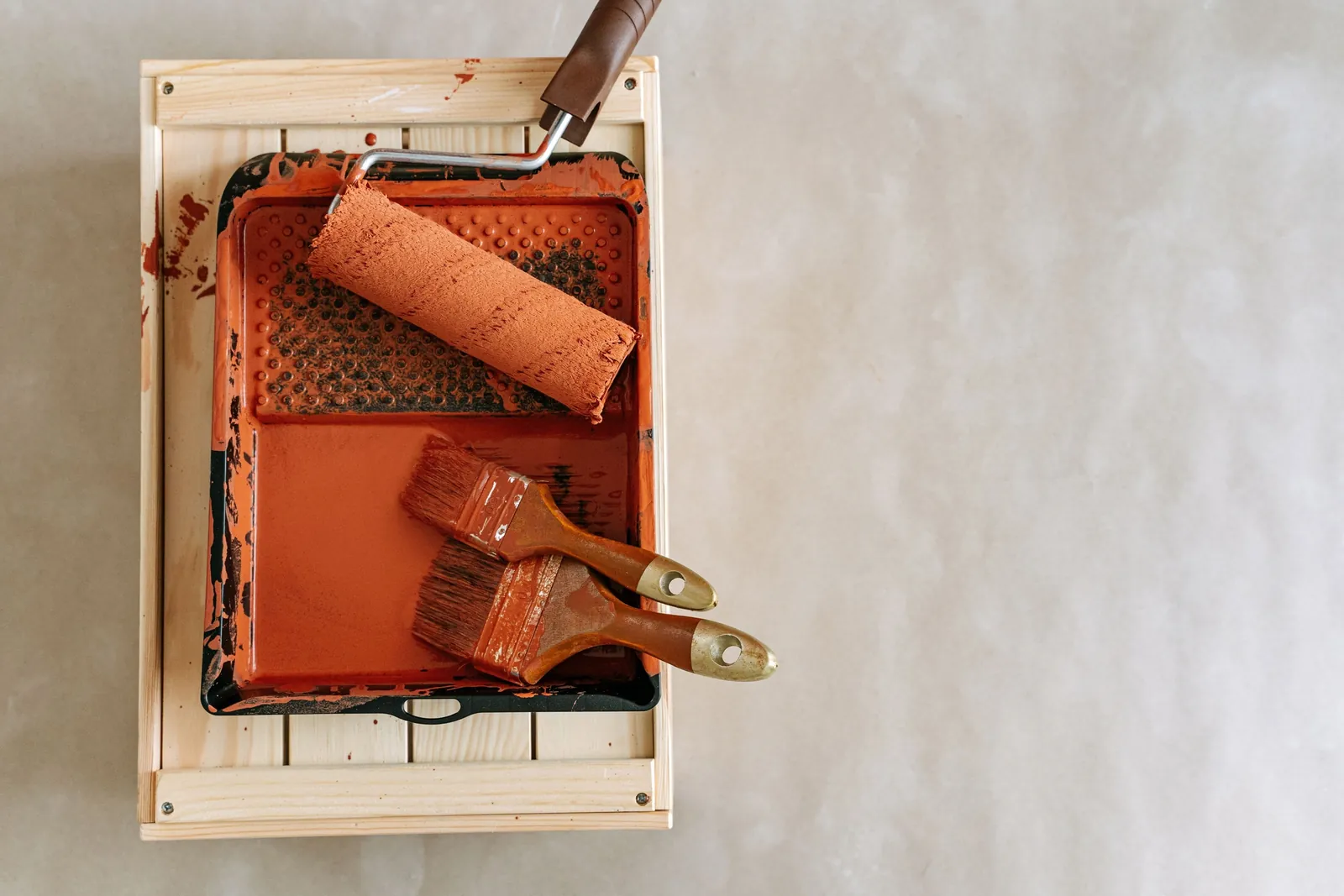Roller and brushes in a paint tray Paint roller and brushes in a tray of orange paint on a wooden crate