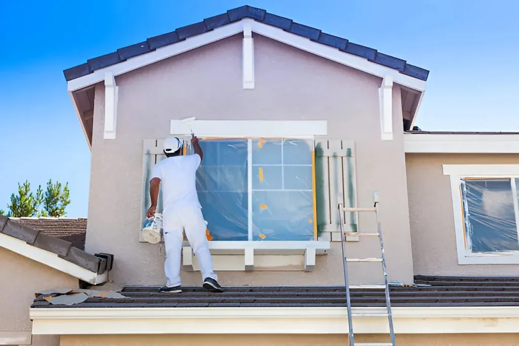 Painting exterior window trim Painter on a roof painting the trim around a second-floor window, with the glass and shutters masked off